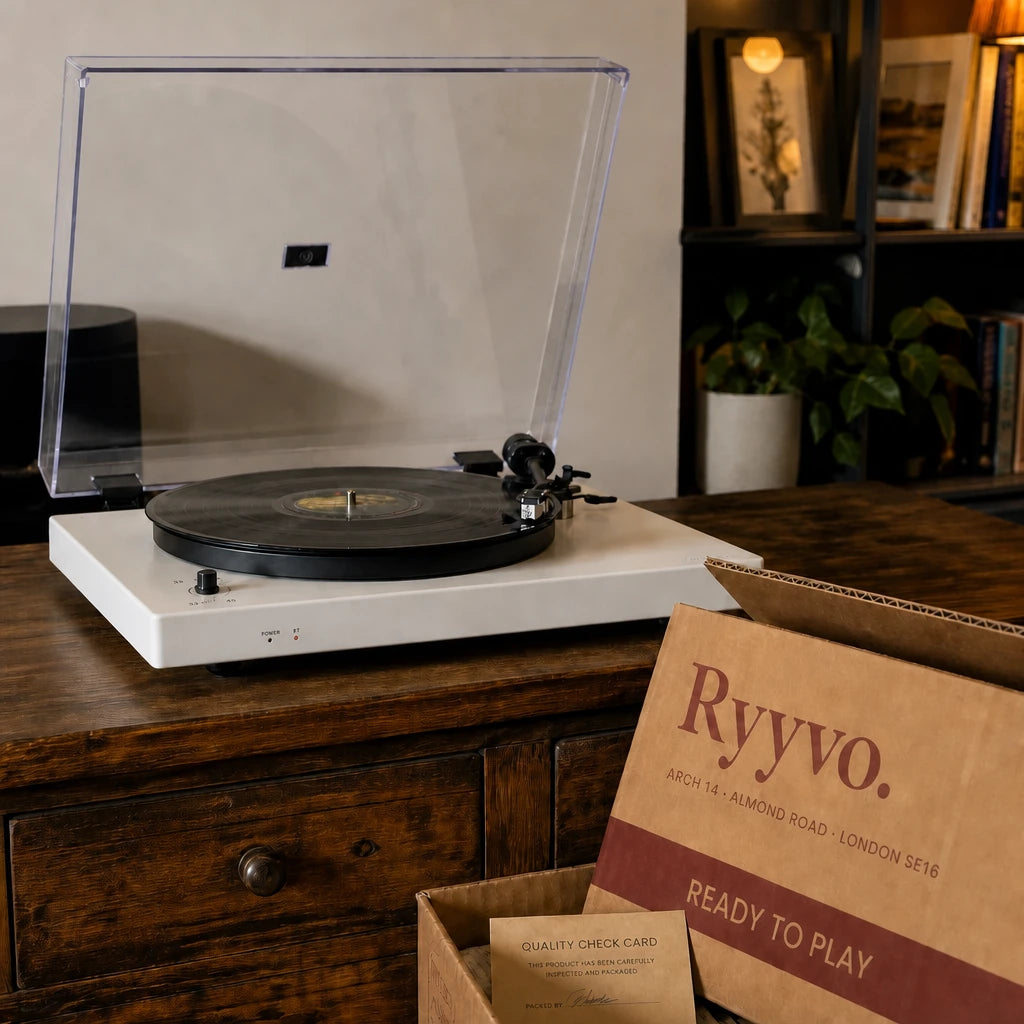 Ryyvo C40 record player in white on a sideboard, dust cover raised, beside the opened Ryyvo carton and its quality check card