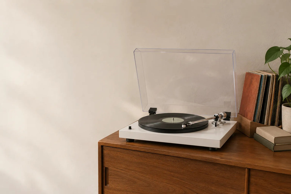 A Ryyvo C40 record player in matte white on a wooden sideboard, dust cover raised and a record on the platter, with records, books and a plant to the right